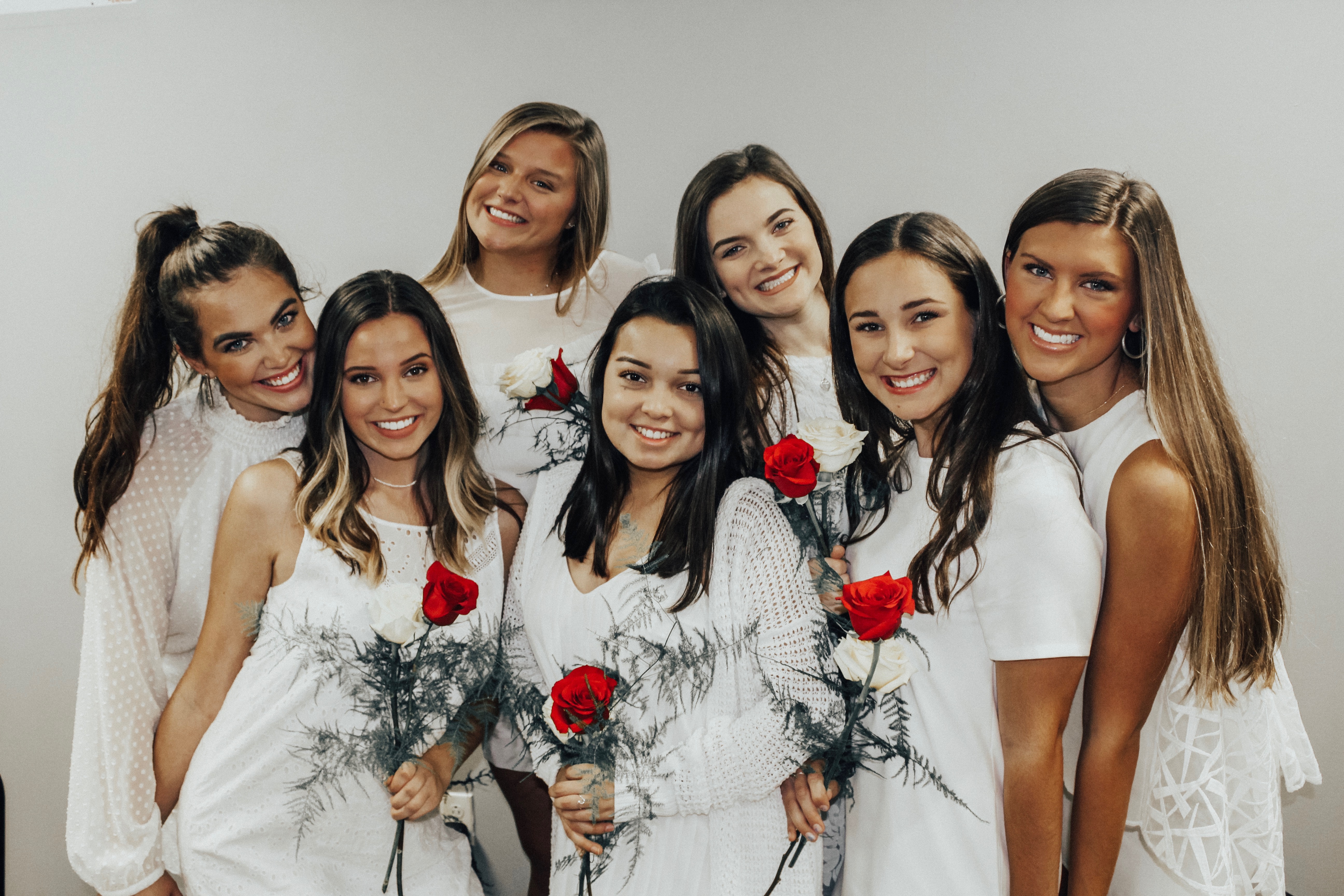 Alpha Gamma Delta member dressed in white dresses, holding red roses and smiling.