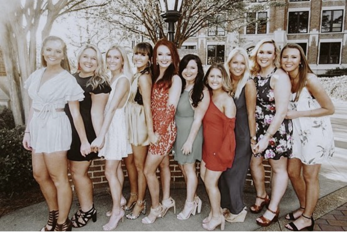 Alpha Gamma Delta members in dresses, holding hands, smiling.